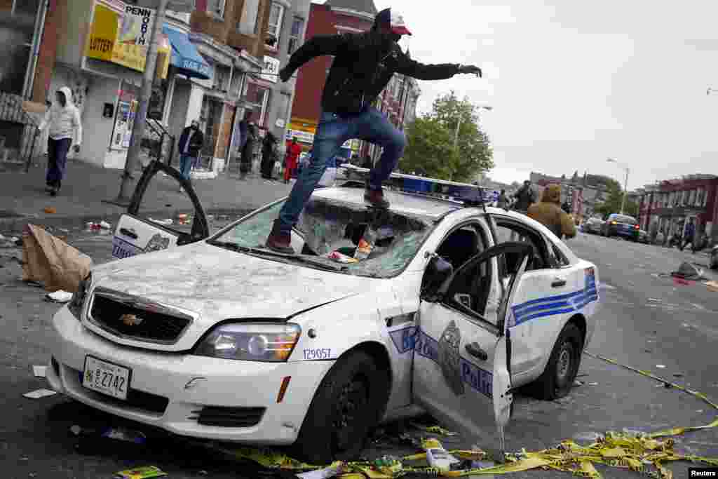 Demonstrators jump on a damaged Baltimore police department vehicle during clashes in Baltimore, Maryland, April 27, 2015.