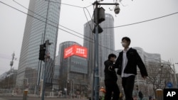 Residents walk past a retail and office district with a screen showing propaganda which reads "Go China! Go Wuhan" as businesses slowly restart in Beijing March 8, 2020.