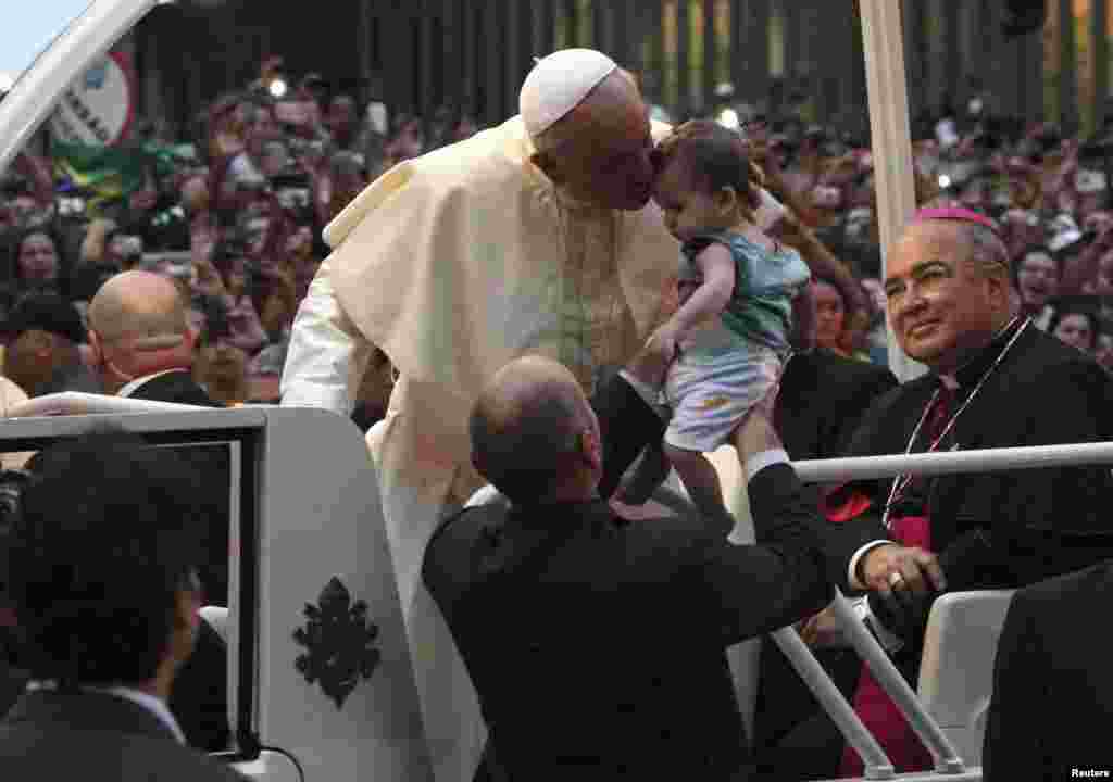 Pope Francis kisses a baby while greeting the crowd of faithful from his popemobile in downtown Rio de Janeiro, July 22, 2013.