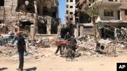 People stand in front of damaged buildings, in the town of Douma, the site of a suspected chemical weapons attack, near Damascus, Syria, April 16, 2018.