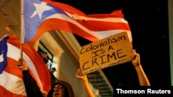 FILE - A man waves a Puerto Rican flag next to a woman who holds a sign during ongoing protests calling for the resignation of Gov. Ricardo Rossello in San Juan, July 23, 2019.