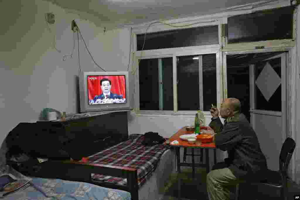 2012年11月8日,一位男士在北京的家里一边吃饭一边观看中共总书记胡锦涛在18大开幕式上发表讲话的新闻。