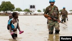 Une fillette tenant un bébé passe devant des soldats de la paix de l'ONU, après que de fortes pluies et des inondations ont forcé des centaines de milliers de personnes à quitter leurs maisons, dans la ville de Pibor, dans l'État de Boma, au Soudan du Sud, le 6 novembre 2019.