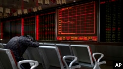 FILE - An investor takes a nap in front of an electronic board displaying stock prices at a brokerage house in Beijing, Monday, Sept. 17, 2018.