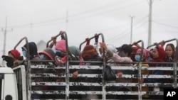 FILE - Garment workers stand on the cargo platform of a truck as they head home after their work shift outside Phnom Penh, Cambodia, Nov. 11, 2020.