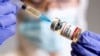 Una mujer sostiene una pequeña botella etiquetada con una etiqueta adhesiva de "Vacuna contra el coronavirus COVID-19" y una jeringa médica.