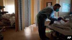 El capellán Elías Mena sostiene la mano de un paciente de COVID-19 mientras ora por él en el Centro Médico Providence Holy Cross, en el sector Mission Hills, de Los Angeles el 15 de enero. 