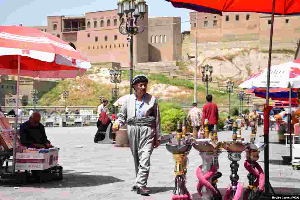 Erbil Kalesi’nin eteğindeki meydanda günlük hayat, sokak satıcıları, minik çay ocakları ve ilk baharda bile rahatsız etmeye başlayan sıcaktan korunmaya çalışanların sığındığı şemsiyeler…