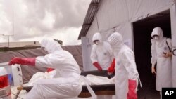 FILE - Health workers wearing protective gear remove the body of a man they suspect died from the Ebola virus at a treatment center on the outskirts of Monrovia, Liberia, Nov. 28, 2014.
