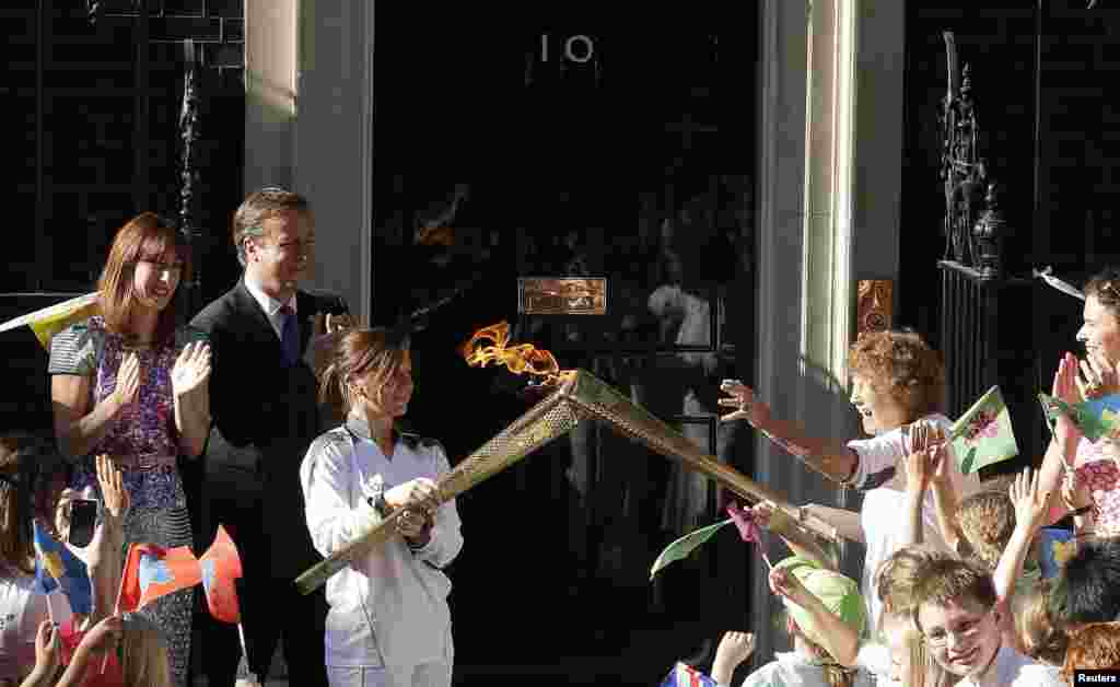 Britain's Prime Minister David Cameron (2nd L) and his wife Samantha (L) look on as Olympic torch bearer Florence Rowe (R) receives the flame from Kate Nesbitt (3rd L) in Downing Street, July 26, 2012.