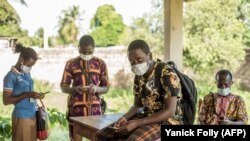 Des agents portant un masque de protection utilisent leur téléphone portable avant une distribution de moustiquaires à Pahou, à 30 km à l'ouest de Cotonou, le 28 avril 2020 avant une distribution de moustiquaires anti-paludisme pendant la pandémie de COVID-19. Pho Yanick Foll/AFP