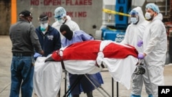 A body wrapped in plastic is unloaded from a refrigerated truck by medical workers wearing personal protective equipment due to COVID-19 concerns, March 31, 2020, at a hospital in New York.