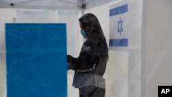 Seorang sukarelawan mengenakan masker, memperagakan bagaimana seorang yang dikarantina akibat terkena virus korona mengikuti pemilihan dalam tenda khusus di sebuah TPS di Tel Aviv, Israel, 1 Maret 2020. (Foto: dok). 