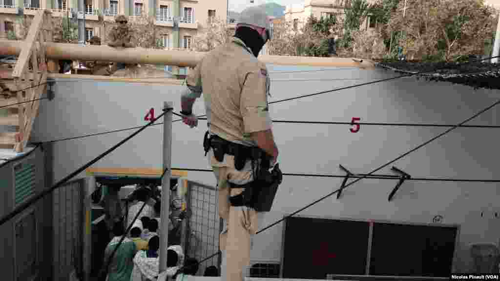 Un militaire norvégien veille sur les migrants qui débarquent du bateau "Siem Pilot" à Messine, Sicile, 6 ocotbre 2015 (Nicolas Pinault/VOA).