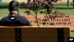 A man sits near a bench memorializing people who died from COVID-19 in Bayonne, N.J., Thursday, May 20, 2021. (AP Photo/Seth Wenig)