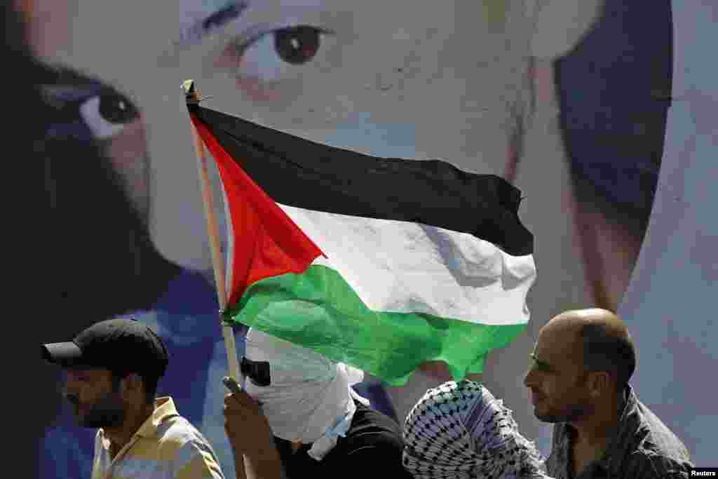 Warga Palestina berdiri di depan poster bergambar Mohammed Abu Khudair, 16, dalam pemakamannya di Shuafat, pinggiran kota Arab di Yerusalem (4/7). (Reuters/Finbarr O'Reilly)
