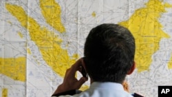 Petugas kepolisian memeriksa peta Indonesia di pusat penanganan krisis yang didirikan oleh otorita lokal untuk pesawat AirAsia QZ8501 yang hilang, di bandara internasional Juanda, Surabaya, 28 Desember 2014.