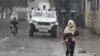 Una mujer camina el 9 de Julio de 2021 bajo la lluvia mientras un vehículo armado transita por las calles cercanas a la Cota 905, en Caracas, Venezuela, una de las comunidades más peligrosas del país suramericano, .