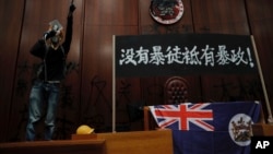 一名進入香港立法會的抗議者站在掛在立法會內的香港殖民地旗幟旁使用擴音喇叭講話。（2019年7月1日） 