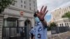 當押送任志強的警車抵達北京第二中級人民法院時一名警察在向記者做手式。 （2020年9月11日）