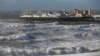 People walks along the shoreline as waves crash onto the beach in Brighton, England, Monday, Oct. 28, 2013. A major storm with hurricane force winds is lashing much of Britain, causing flooding and travel delays with the cancellation of many flights and 