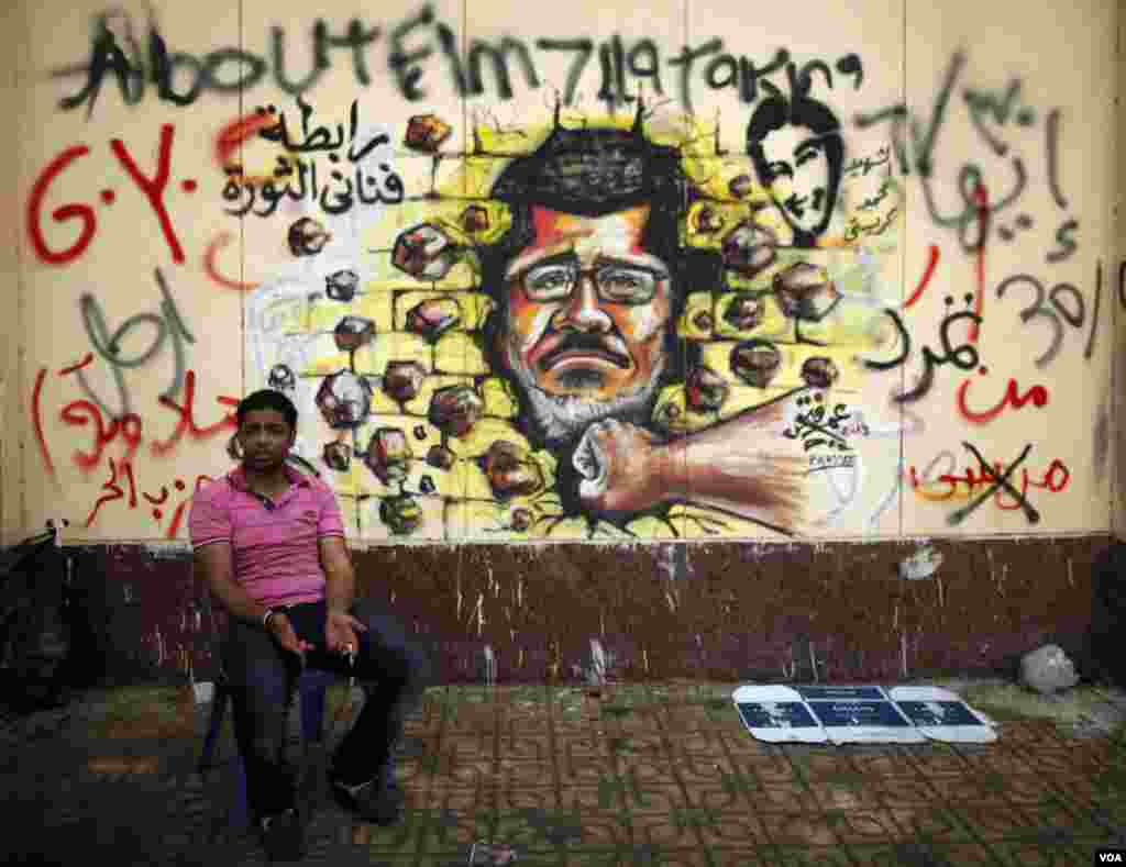 A protester, opposing Egypt's President Mohamed Morsi, sits next to graffiti depicting Morsi on a wall in Cairo July 2, 2013.