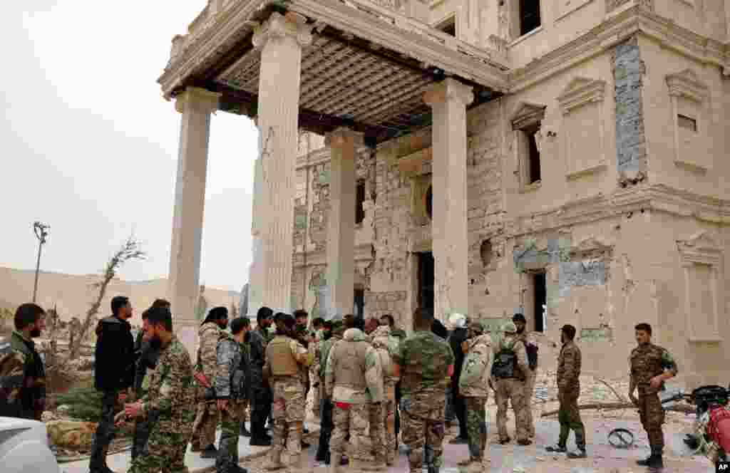 In this photo released on March 24, 2016, by the Syrian official news agency SANA, Syrian government soldiers gather outside a damaged palace, in Palmyra, central Syria.