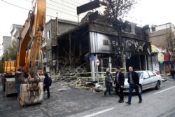 People walk near a burnt bank, after protests against increased fuel prices, in Tehran, Nov. 20, 2019.