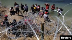ARCHIVO - Migrantes aguardan detrás de los alambres de púas tras cruzar el Río Grande hacia Estados Unidos en Eagle Pass, Texas, EEUU, el 28 de septiembre de 2023.