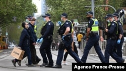 People carry their shopping as police patrol in Melbourne, Australia, Sept. 30, 2021, as the city grapples with a surge in COVID-19 infections.